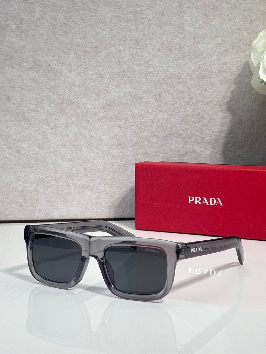 Prada sunglasses with gray rectangular frame and dark lenses, logo on arms.