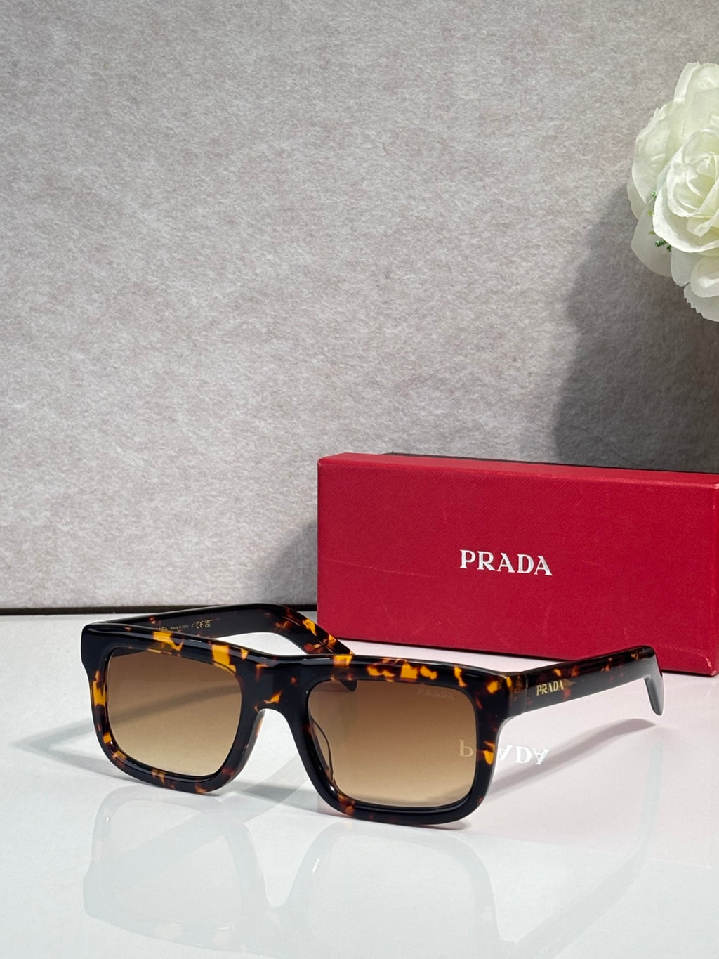 Prada sunglasses with tortoiseshell oversized square frame and dark lenses, logo on arms.
