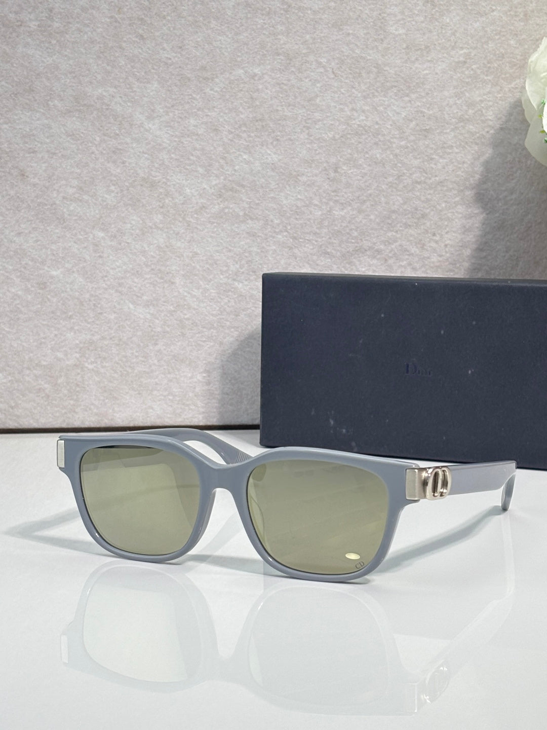 Dior sunglasses with muted blue frames, green tinted lenses, and gold logo hinge detail