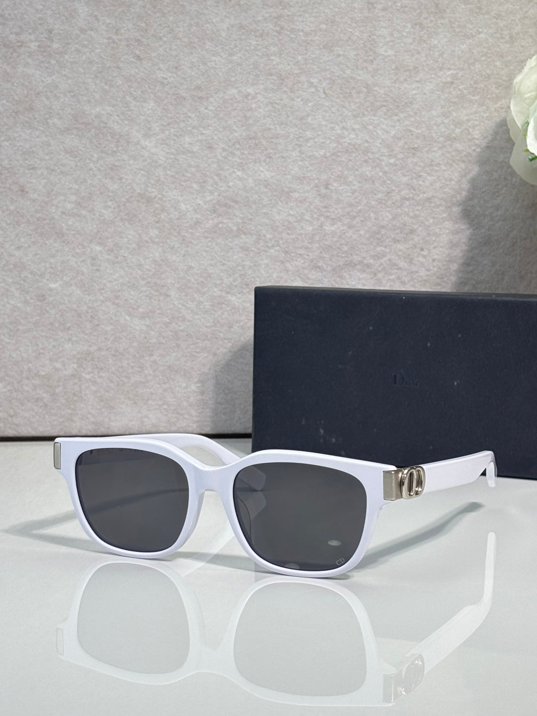 Dior sunglasses with white frames, dark tinted lenses, and gold logo hinge detail