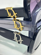 Close-up of black sunglasses with gold 'D' logo on the temple