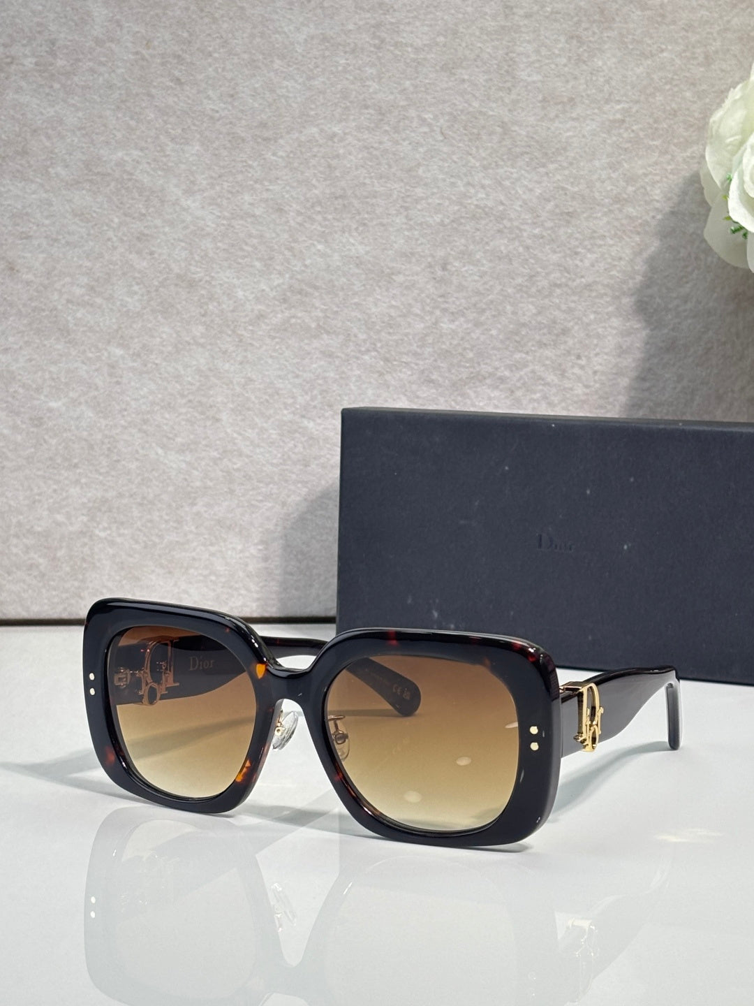 Black square sunglasses with amber-tinted lenses and gold hinge detail