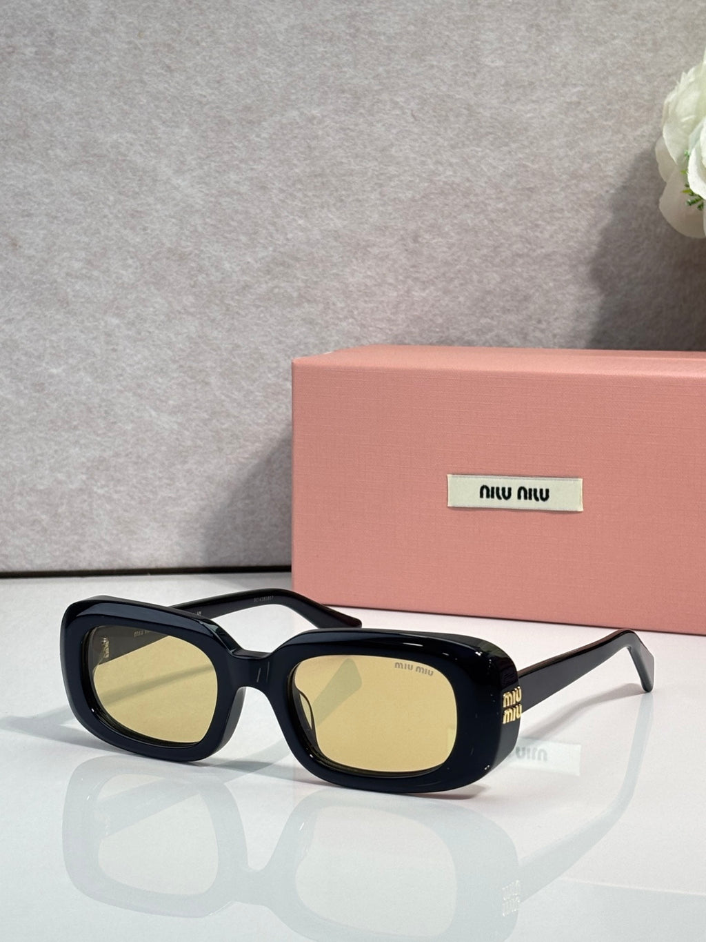Glasses with dark frame and yellow-tinted lenses, rectangular with side logos