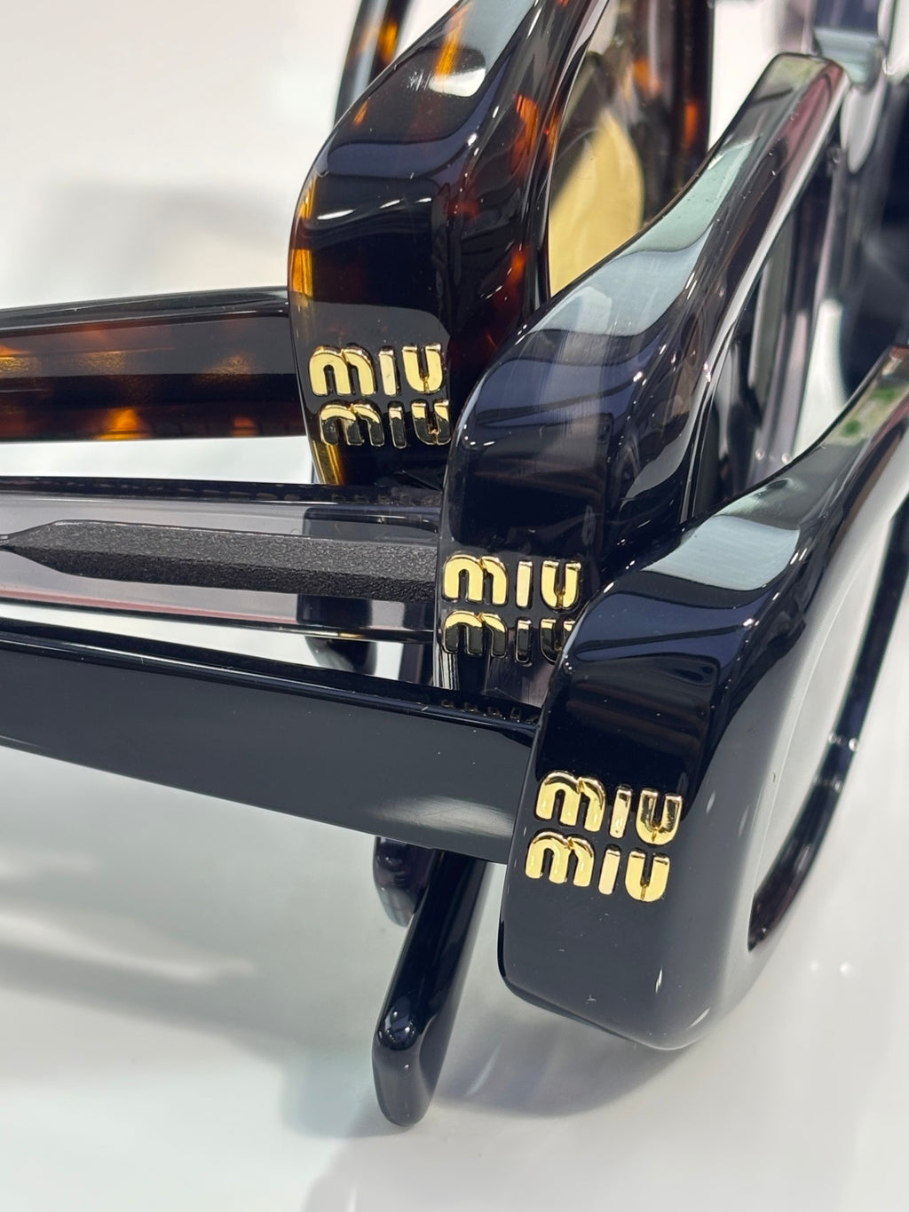 MiuMiu glasses temple close-up: gold 'miu miu' logos on black arms
