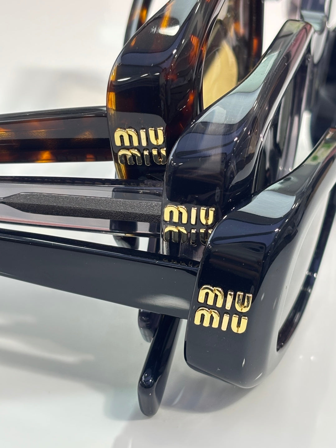 MiuMiu glasses temple close-up: gold 'miu miu' logos on black arms