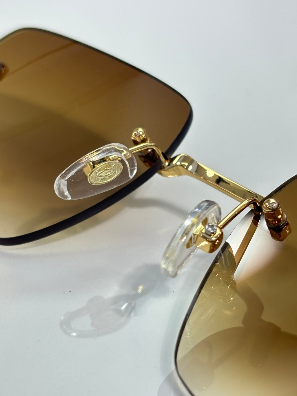 Cartier sunglasses close-up with gold frame and amber-tinted lenses, decorative hinge detail.