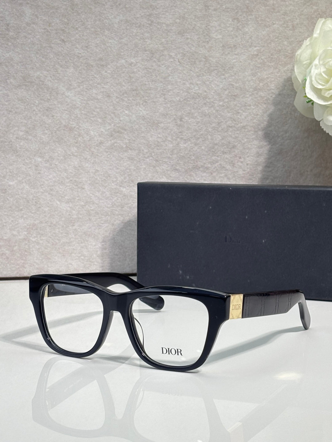 Black eyeglass frame with square lenses, white inner detail, gold temple logo