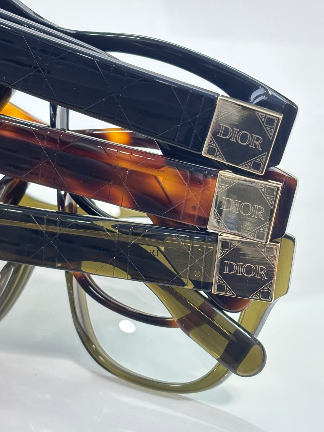 Close-up of stacked tortoiseshell and dark frames with gold-tone Dior hinges