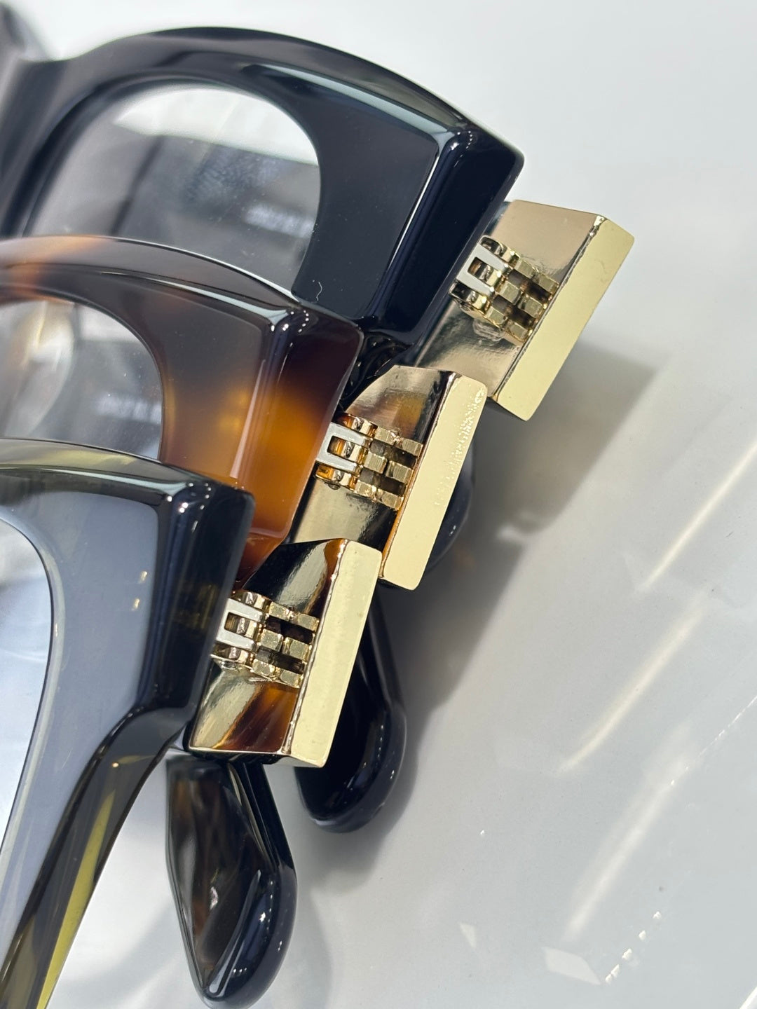 Close-up of dark eyeglass temple hinge with gold-tone detail and frame curvature