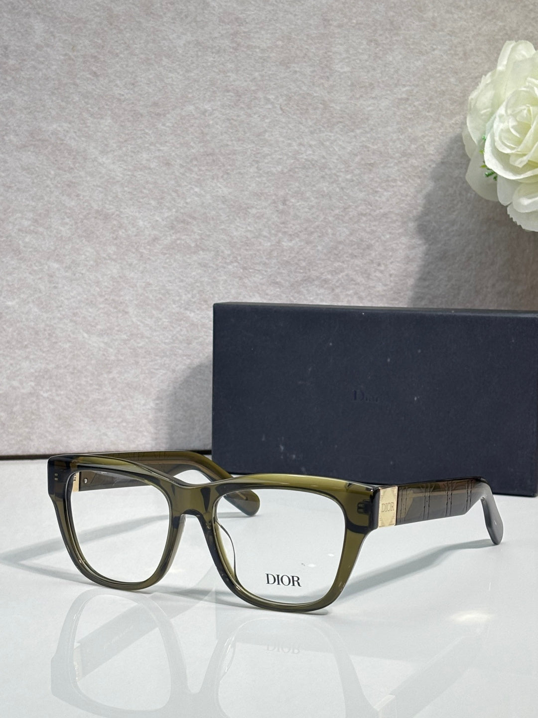 Olive-green eyeglass frame with square lenses, gold temple logo details