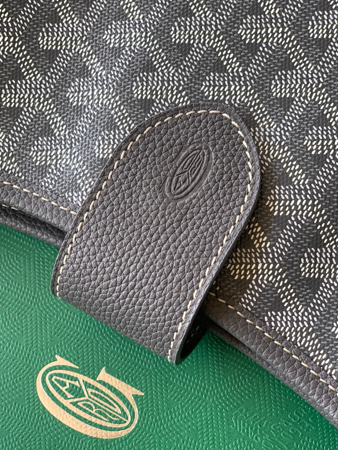Goyard monogram bag leather tab detail with embossed circular emblem, dark gray