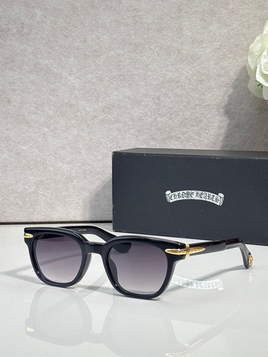 Glasses with black frames, dark lenses, and gold-tone temple accents.