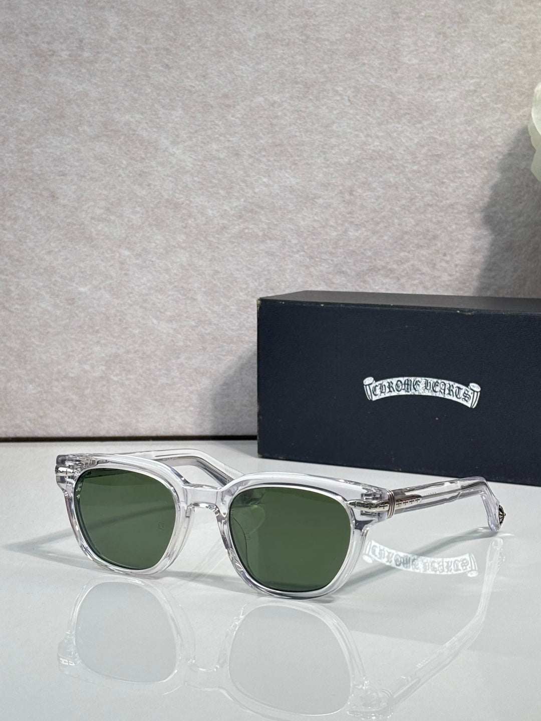 Glasses with clear frames and green-tinted lenses, with engraved temple detailing.