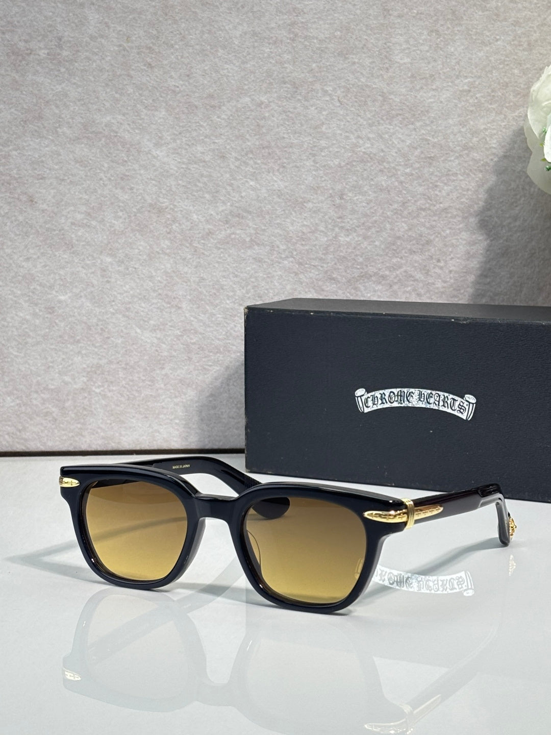 Glasses with black frames and amber-tinted lenses, with gold-tone temple accents.