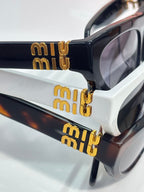 Close-up of black sunglasses with gold miu miu lettering and dark lenses.