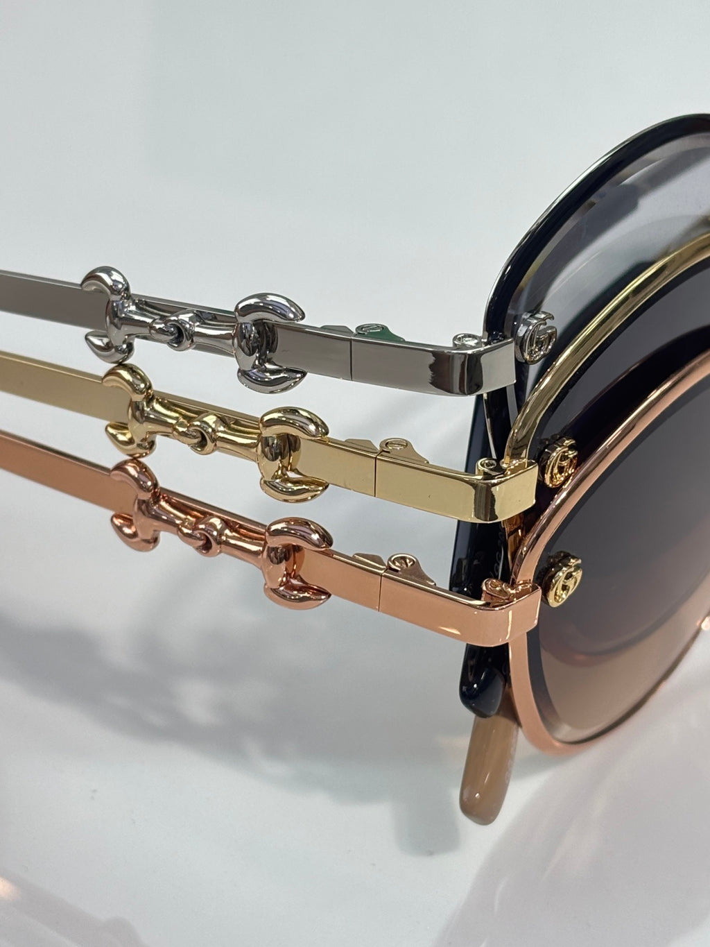 Sunglasses temple close-up with gold and brown chain hardware and dark lens edge