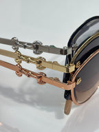 Sunglasses temple close-up with gold and brown chain hardware and dark lens edge