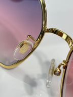 Gucci sunglasses close-up of gold frame hinge with pink-tinted lens.