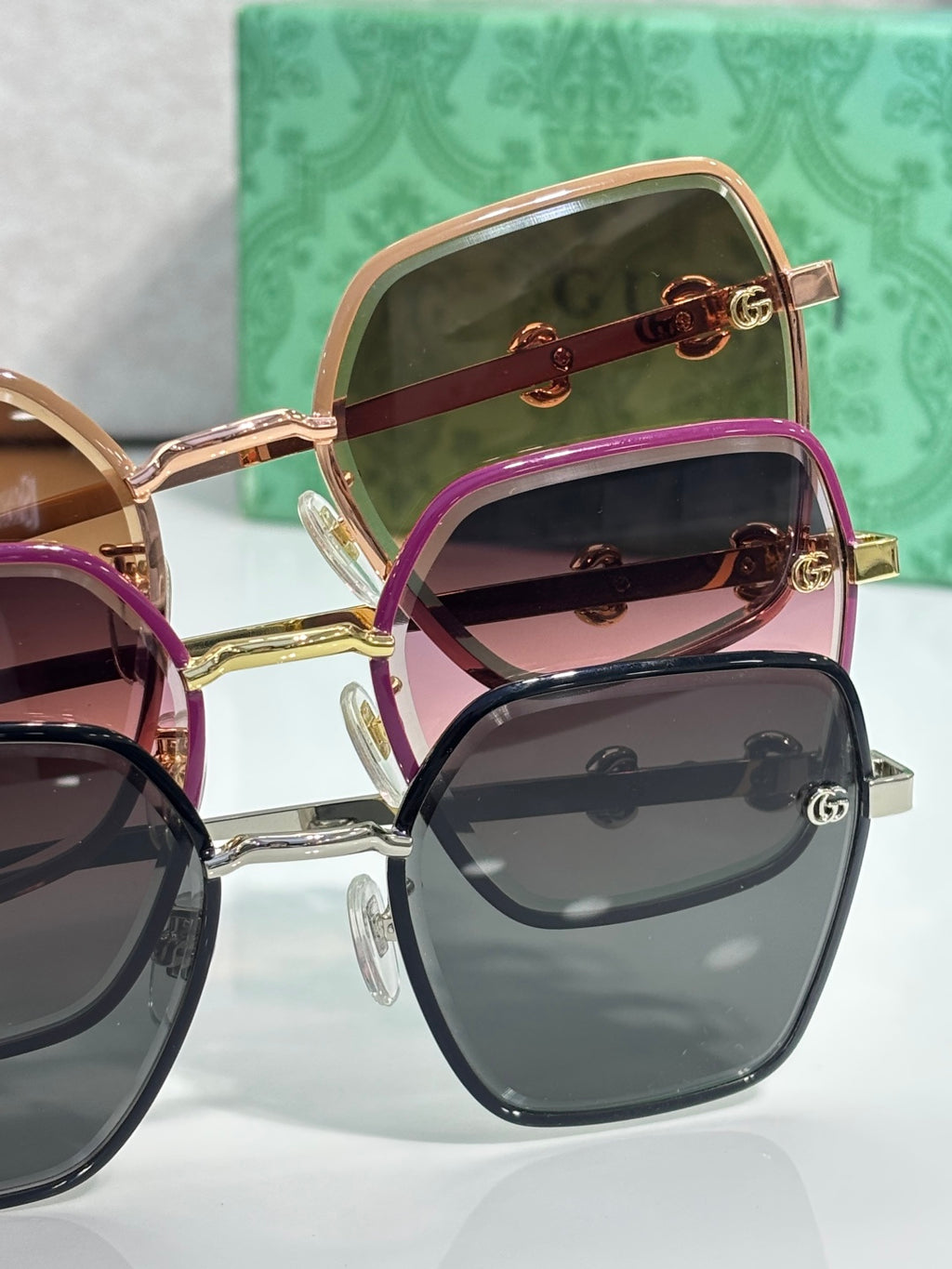 Gucci sunglasses multiple styles stacked: gold frames, dark lenses, pink-tinted lenses.