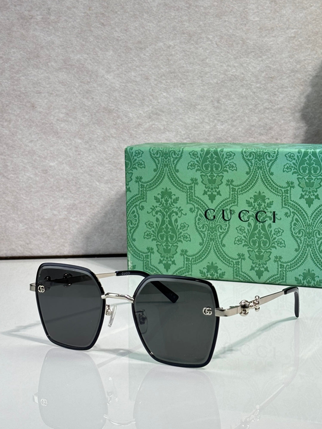 Gucci sunglasses with black frames and gray gradient lenses, square corners.