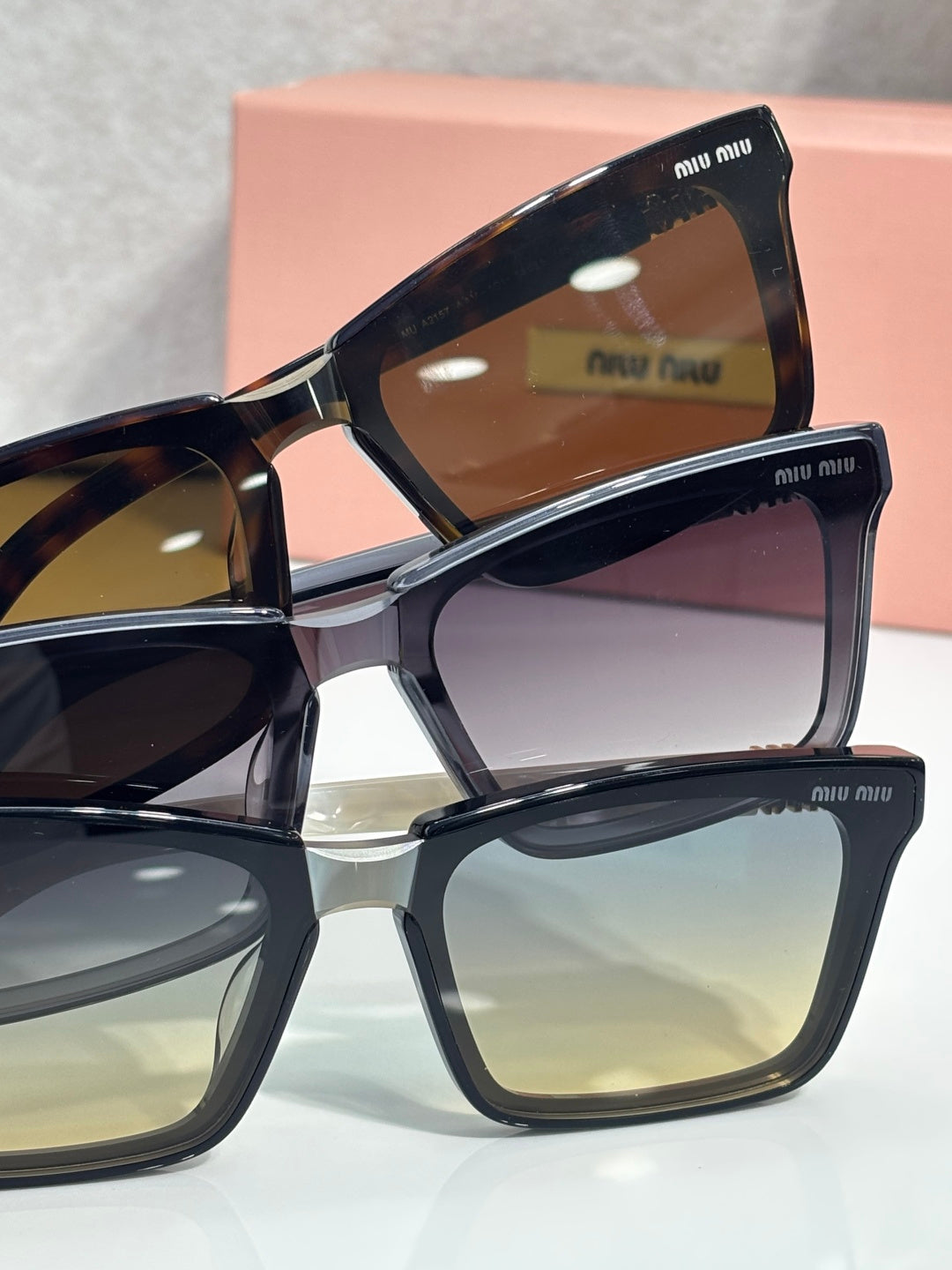 Stacked rectangular sunglasses with black frames and assorted tinted lenses, miu miu logos