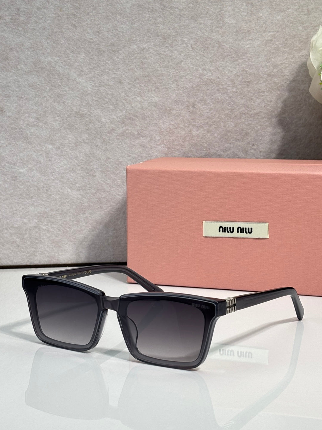 Rectangular dark-tinted sunglasses with black frame and miu miu logo on lens