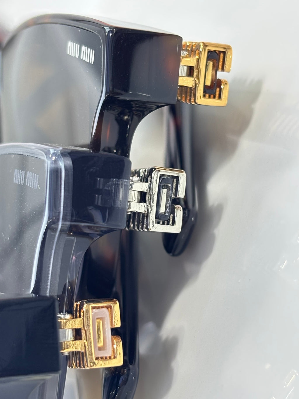 Sunglasses temple detail with black frame and gold-and-silver emblem accents