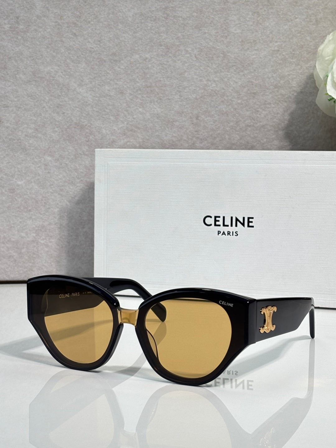 Celine sunglasses with black frames and warm amber lenses, gold logo on temple.