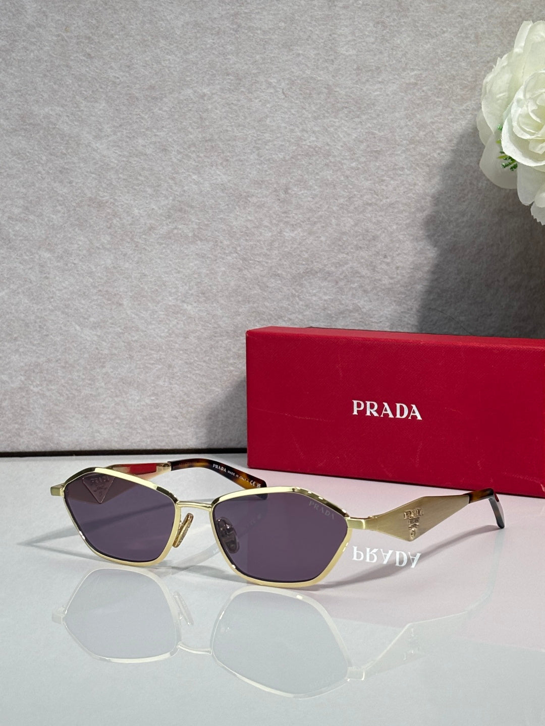 Prada cat-eye sunglasses with gold frame and dark purple lenses, logo on arms