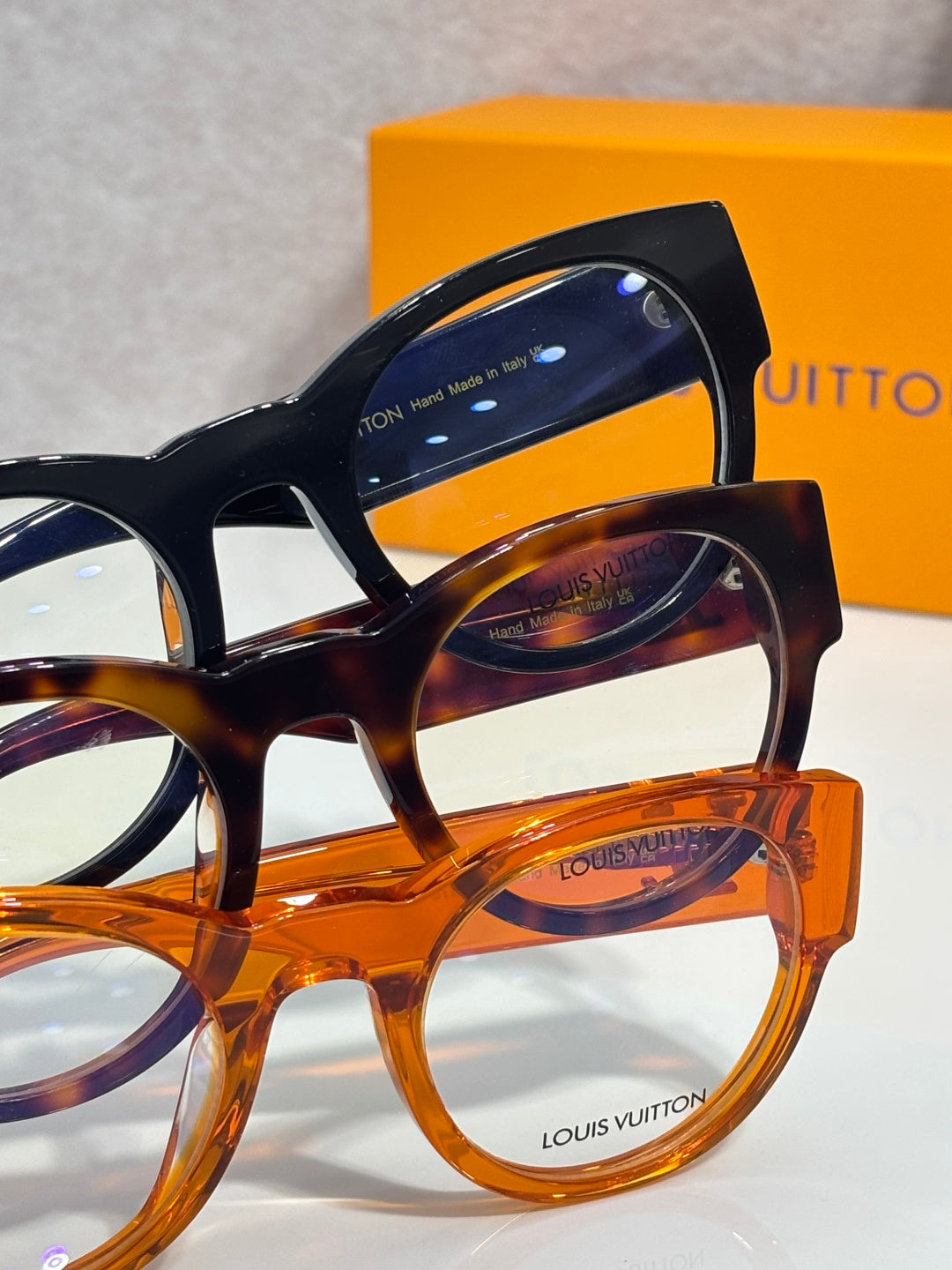 Close-up of stacked eyeglasses: black, tortoise, and orange frames
