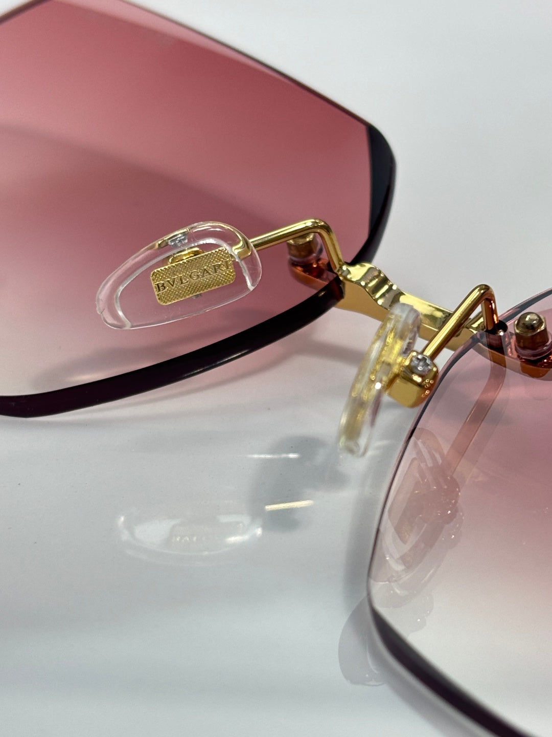 Gold metal sunglasses with purple-pink lenses, close-up of temple detail