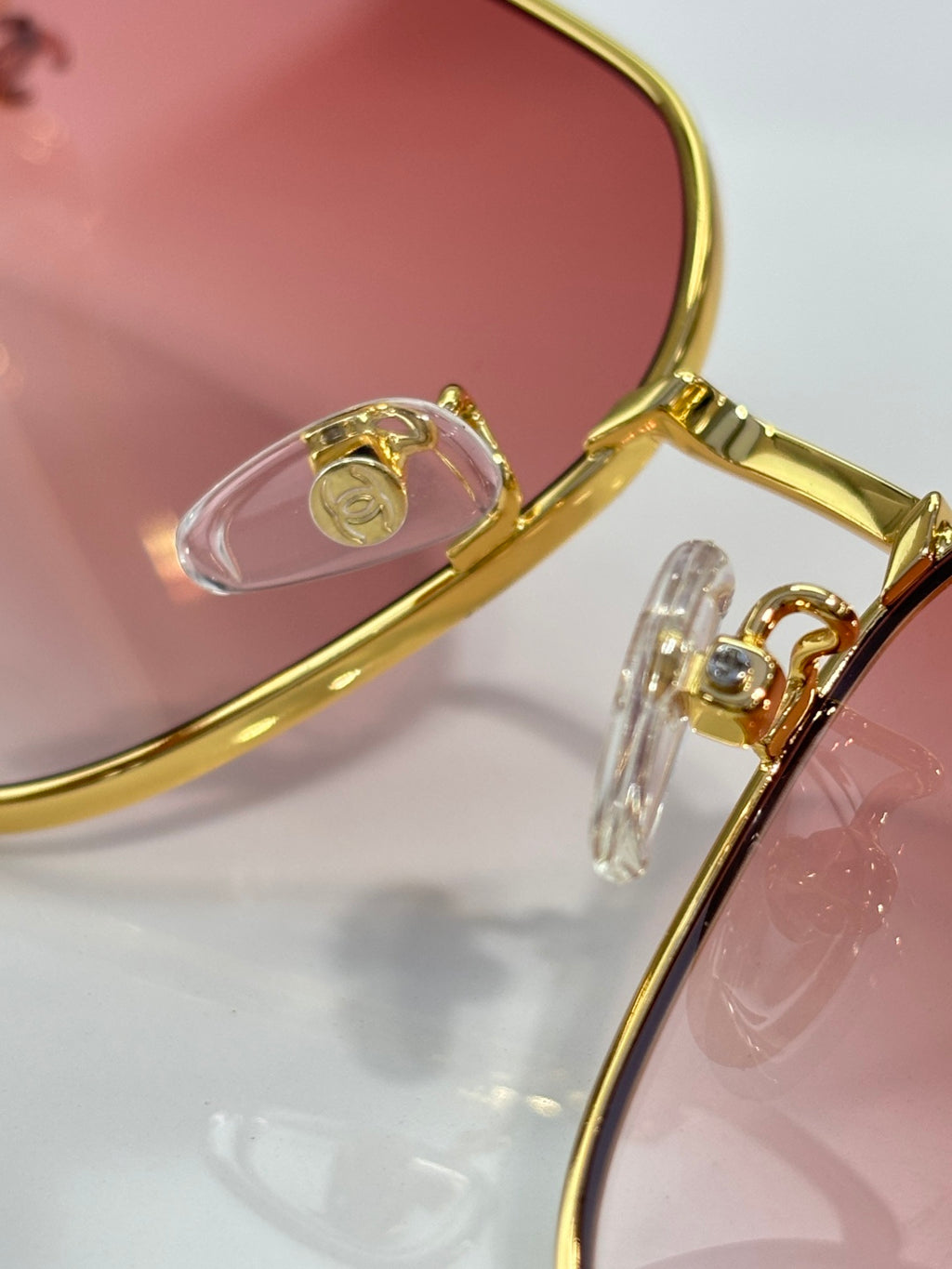 Gold-tone eyeglasses hinge detail with pink tinted lens and metal temple