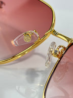 Gold-tone eyeglasses hinge detail with pink tinted lens and metal temple