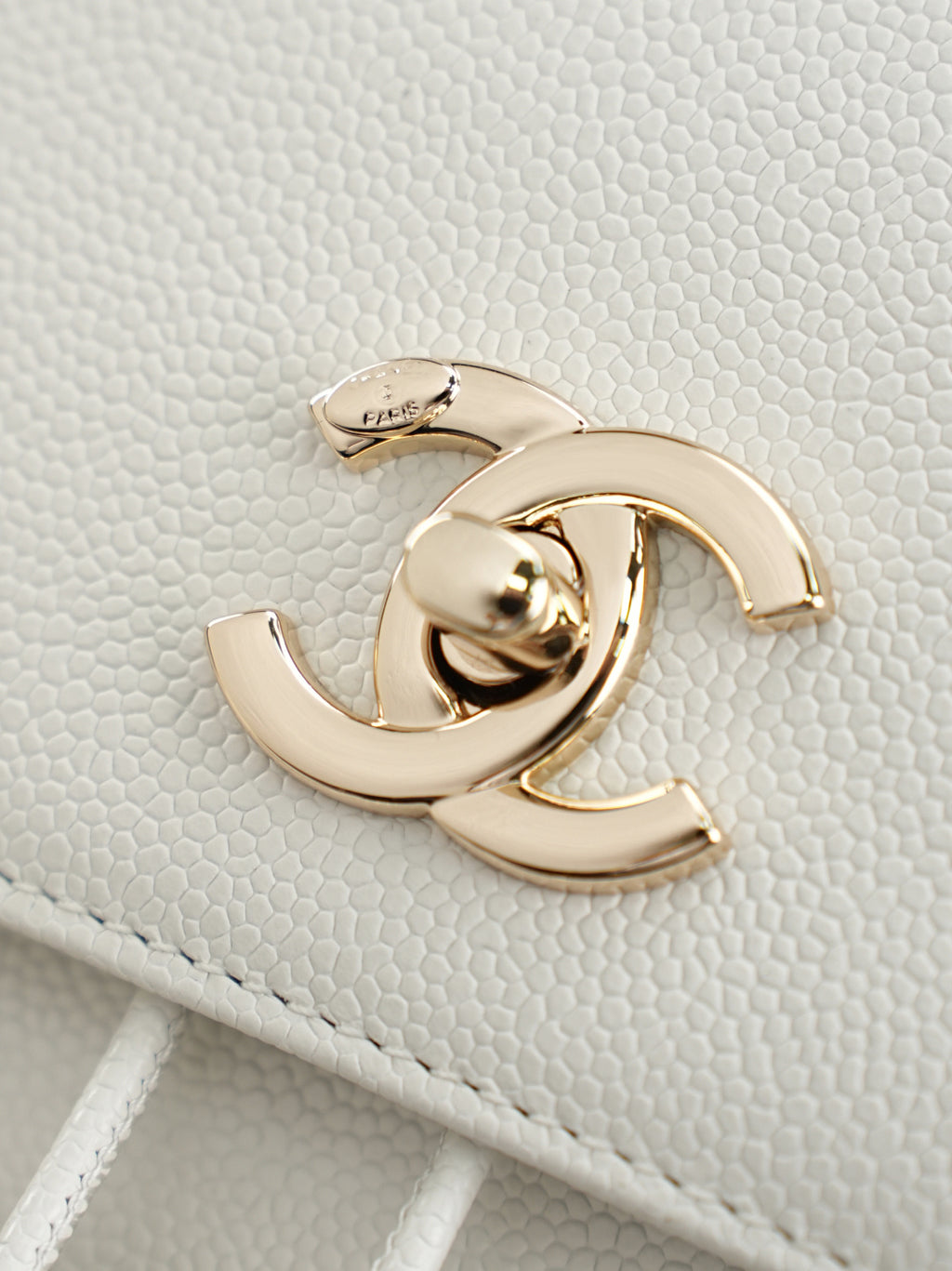 Gold-tone Chanel logo hardware on white textured leather bag flap
