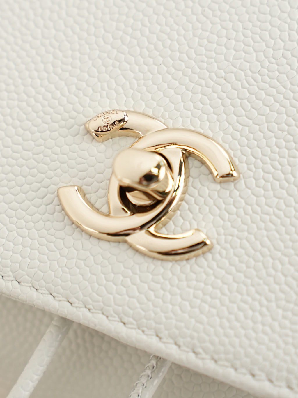 Close-up of gold-tone logo hardware on white quilted bag