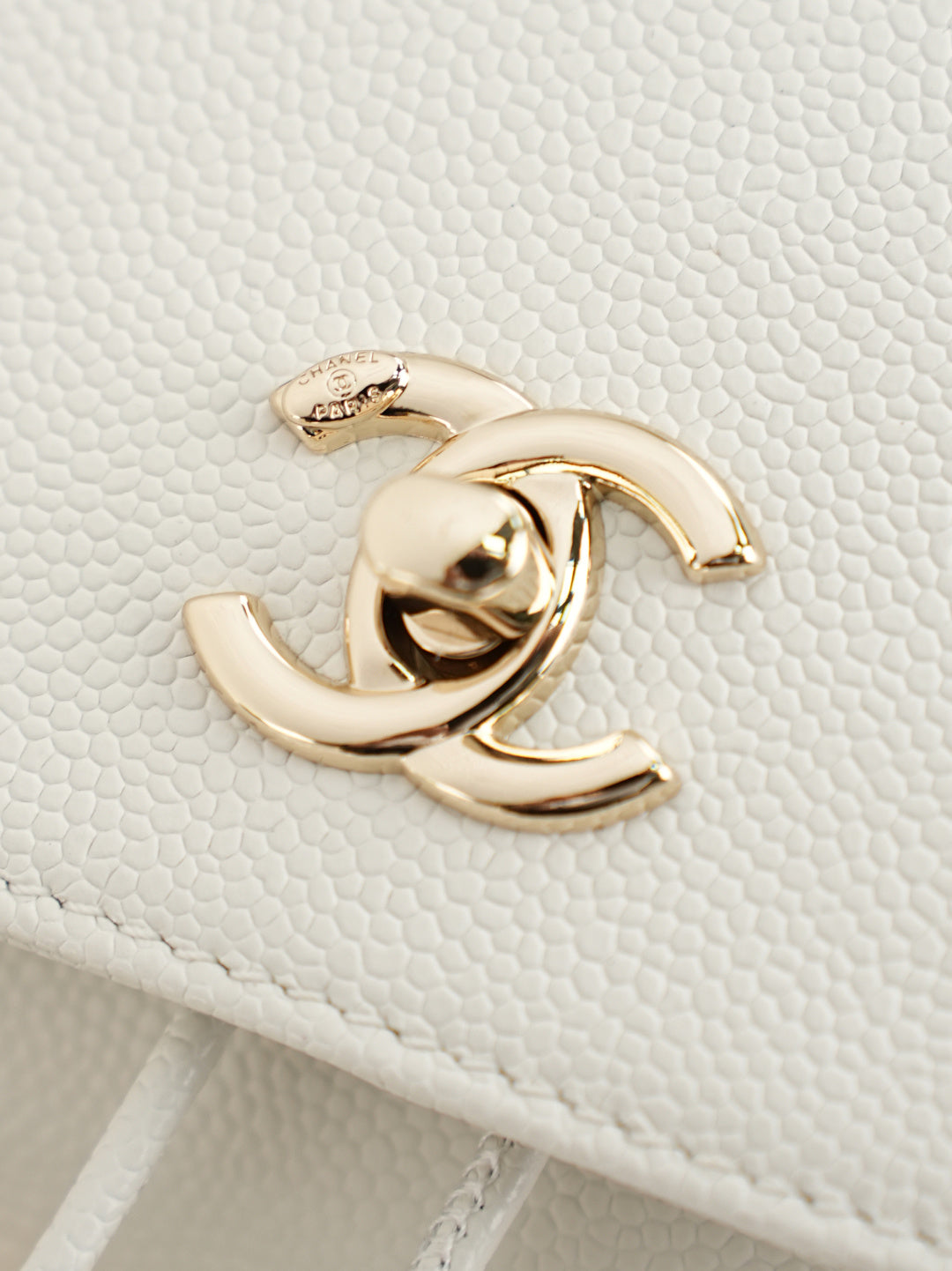 Close-up of gold-tone logo hardware on white quilted bag
