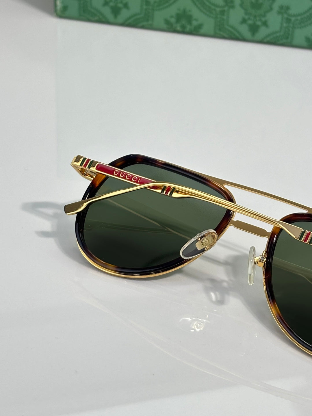 Sunglasses with green lenses and gold frame, red and green striped temple bar detail