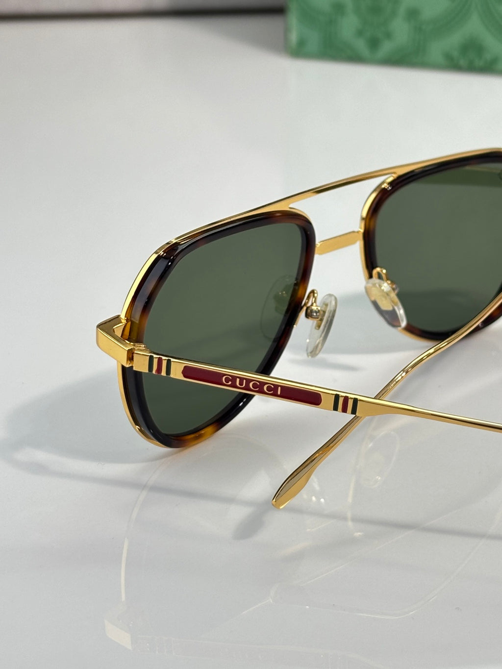 Oval sunglasses with green lenses, gold frame, and red and green striped temple detail