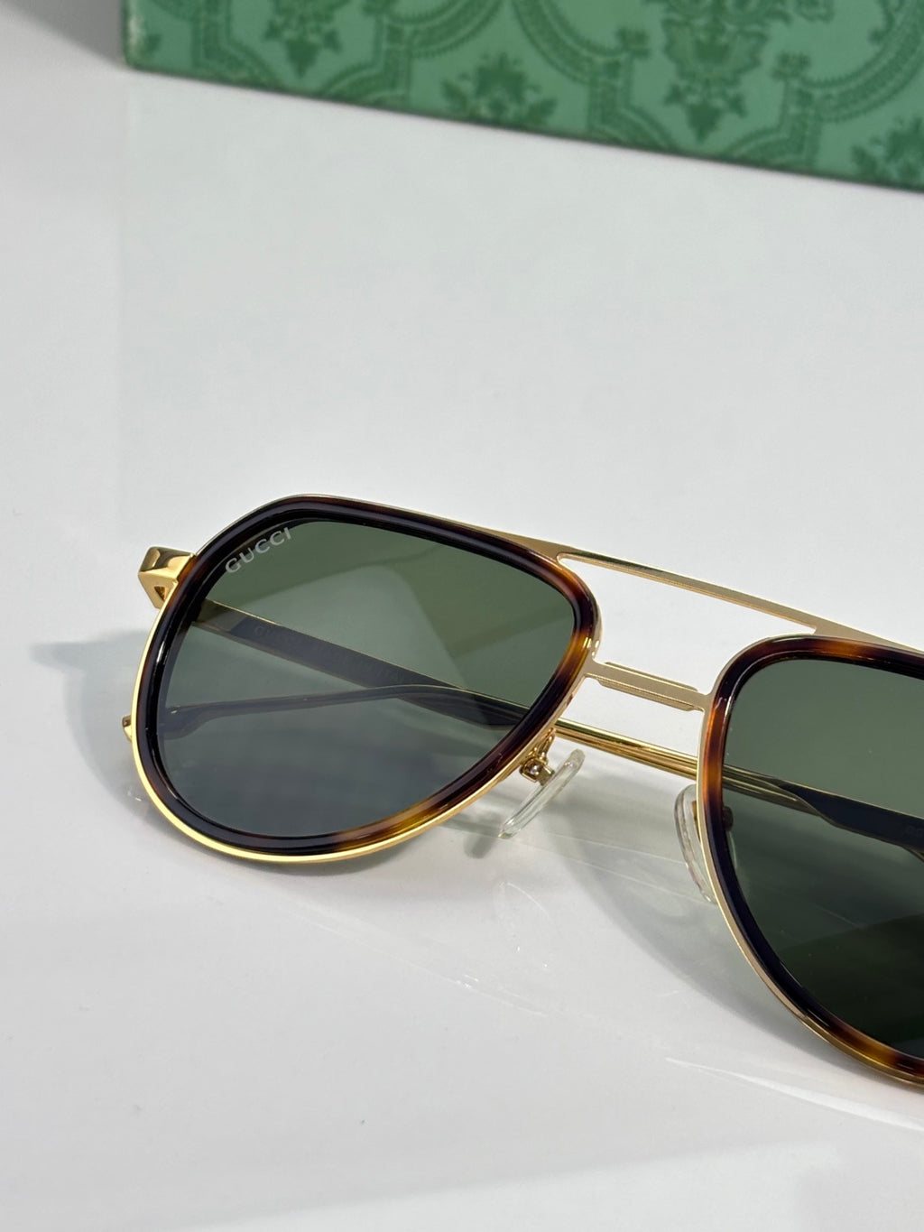 Gucci sunglasses angled view with green lens and gold frame, dark tortoiseshell rim