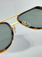 Close-up of gold bridge and temple hinge on tortoiseshell-trim sunglasses with green lens