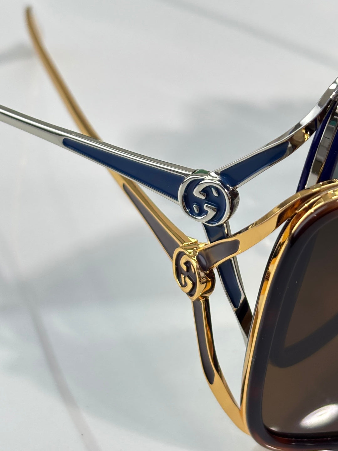 Sunglasses temple detail with blue and gold metal arms and Gucci-style emblem