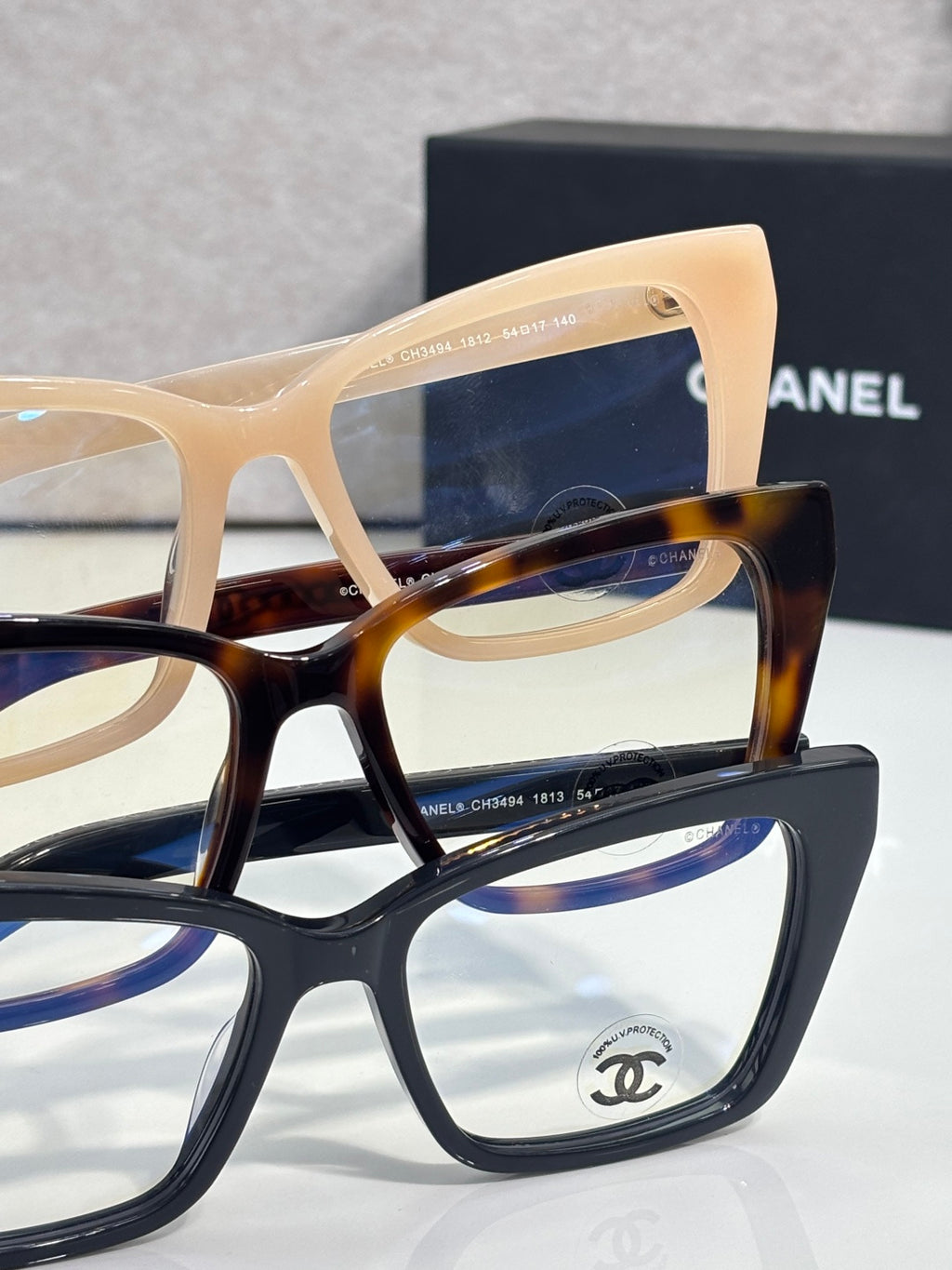 Chanel eyeglasses stack showing tan and dark frames, with gold chain temple detail