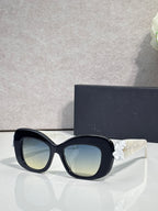 Black Dior glasses with rounded square lenses and white floral charm on the temple.