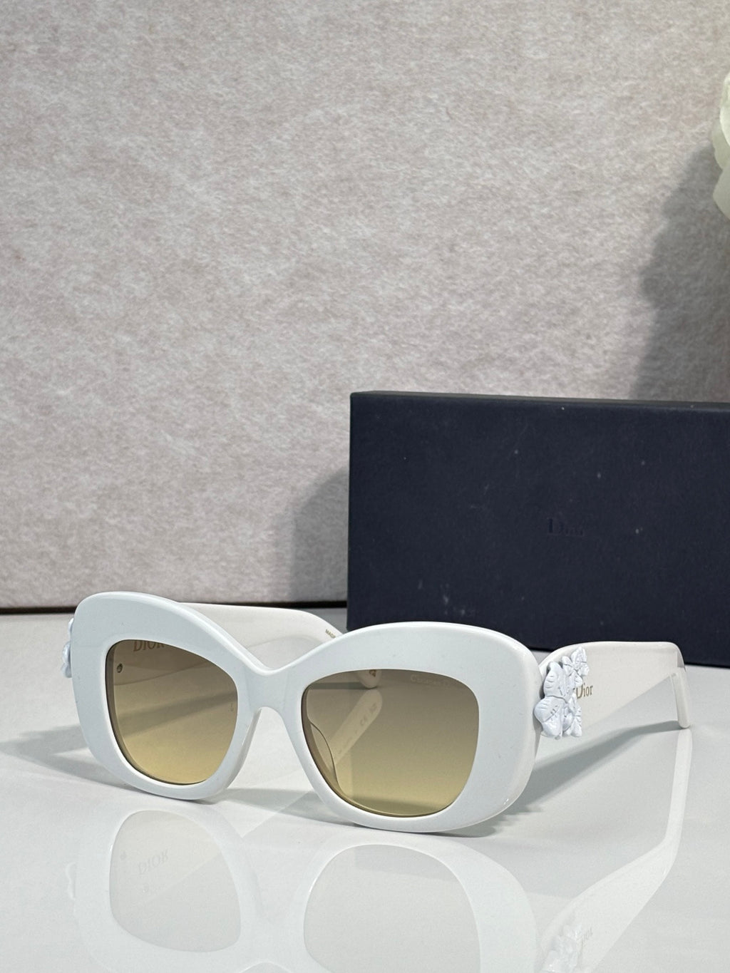 White Dior glasses with rounded square lenses and gold floral charm on the temple.