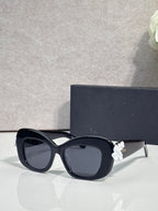 Black Dior glasses with rounded square lenses and white floral charm on the temple.