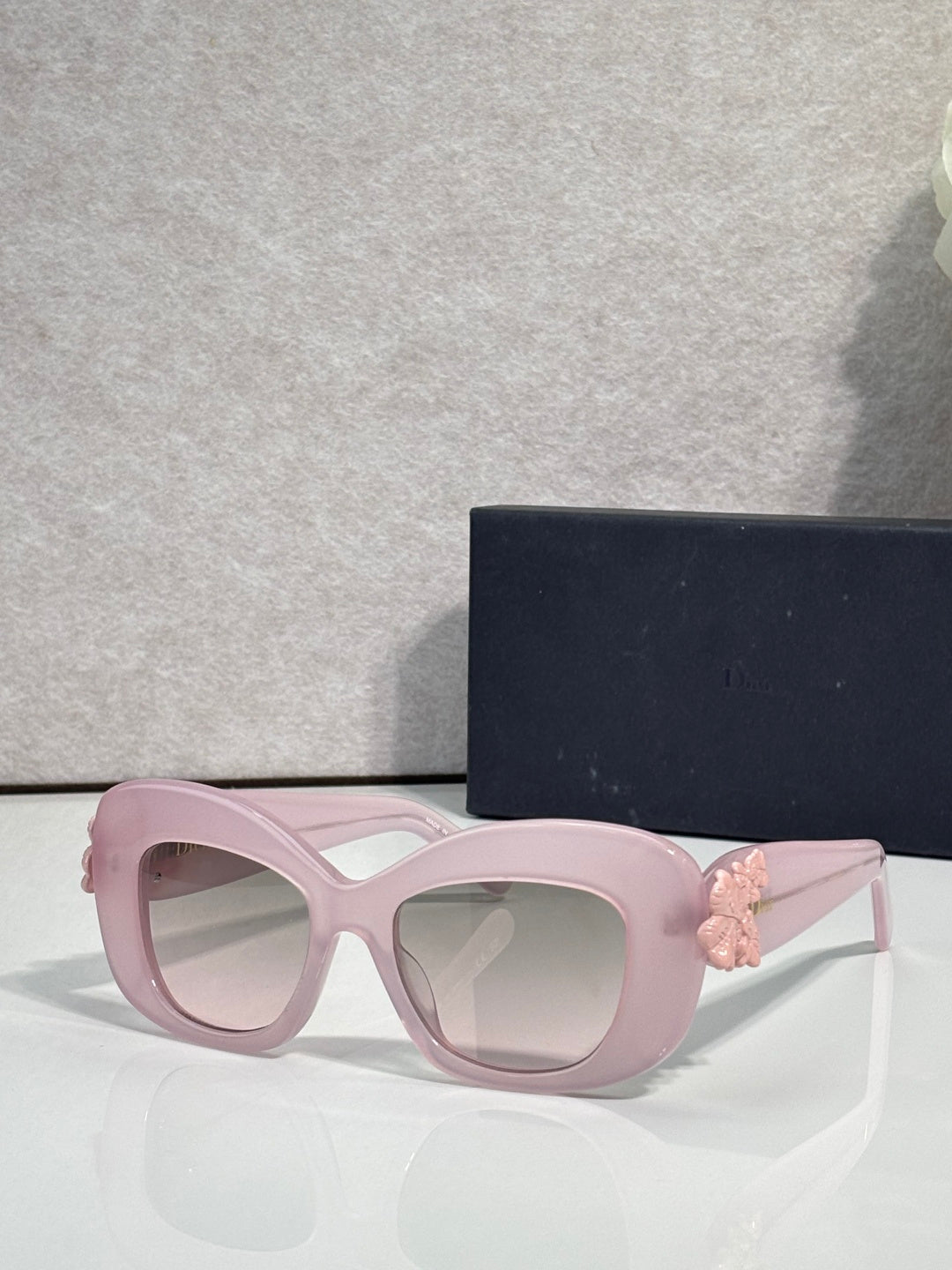 Light pink Dior glasses with rounded square lenses and pink floral charm on the temple.