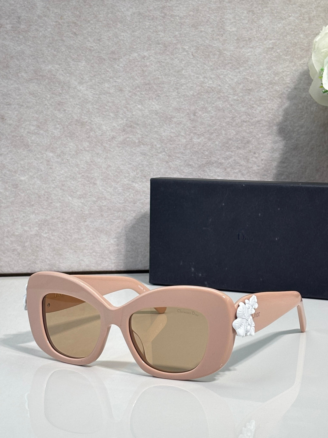 Blush Dior glasses with rounded square lenses and white floral charm on the temple.