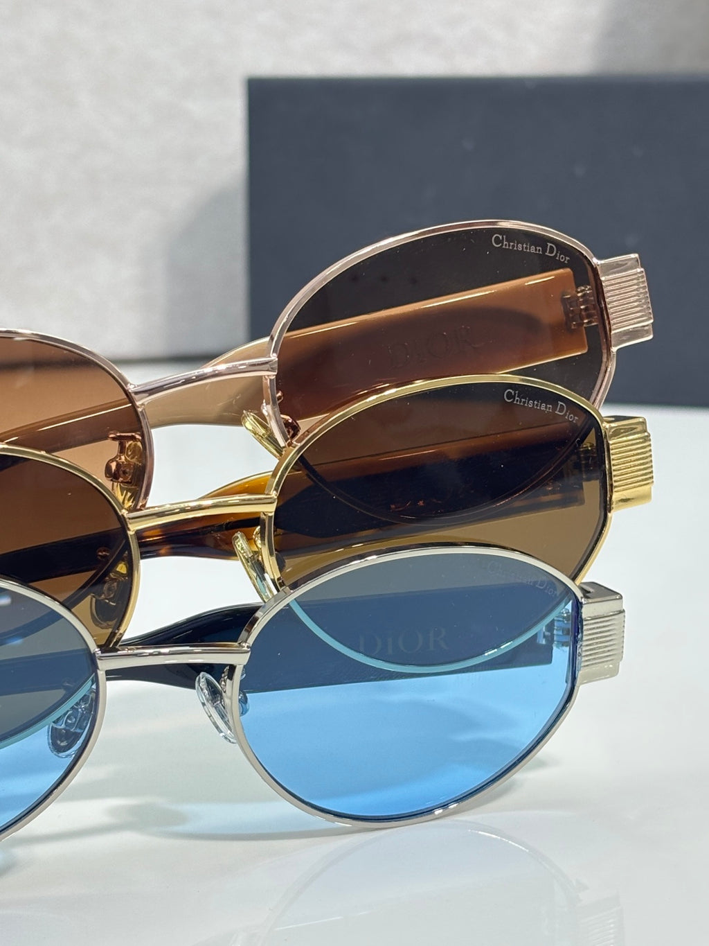 Stacked Dior sunglasses with gold frames, brown and blue tinted lenses, temple text