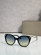 Sunglasses, dark teal rounded frames with gold-tone temple tips and tinted lenses
