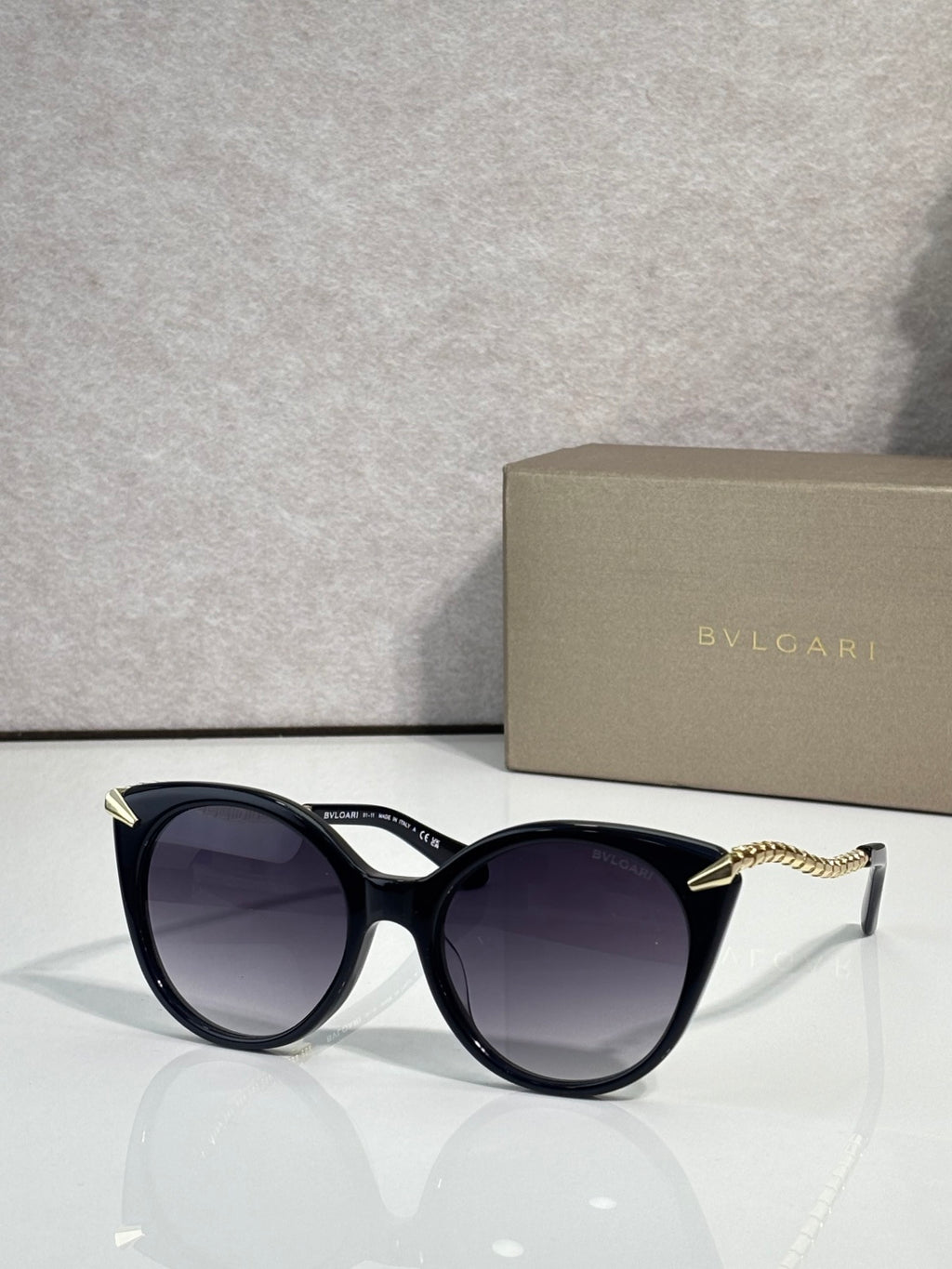 Sunglasses, black rounded frames with gold-tone temple tips and dark tinted lenses
